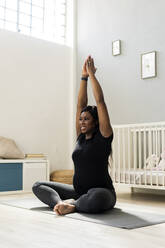 Glückliche schwangere junge Frau mit erhobenen Händen beim Yoga im Schlafzimmer - GIOF13170