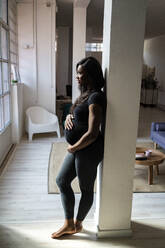 Schwangere Frau lehnt zu Hause an einer Säule - GIOF13179