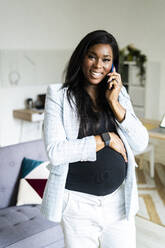 Glückliche schwangere Geschäftsfrau, die mit dem Smartphone spricht, während sie mit der Hand auf dem Bauch steht - GIOF13194