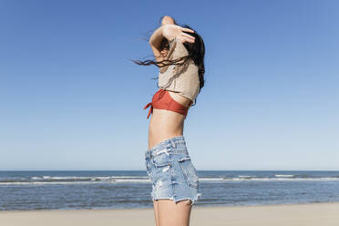 Young woman removing clothes at beach stock photo