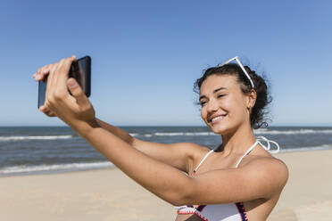 Beautiful woman taking selfie through smart phone at beach - JRVF01415