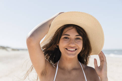 Schöne Frau mit Sonnenhut lächelt, während sie am Strand genießt - JRVF01421