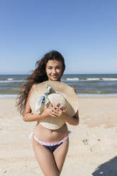 Young woman holding sun hat at beach - JRVF01422