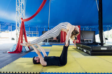 Male artist lifting female athlete on legs and hands at circus - MEUF03791