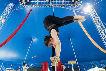 Weibliche Akrobatin beim Üben eines Handstandes mit Sportlern im Hintergrund - MEUF03792