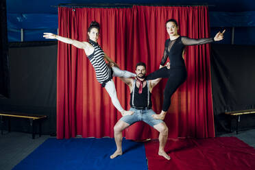 Weibliche Darstellerin streckt sich, während sie auf einem männlichen Akrobaten im Zirkus steht - MEUF03812