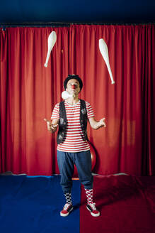 Male performer juggling pins while performing in circus - MEUF03821