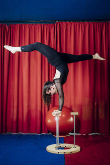 Weibliche Artistin, die im Zirkus einen Handstand mit dem Stock macht - MEUF03826
