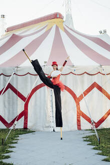 Künstlerin hält Handfächer, während sie mit Stelzen vor einem Zelt steht - MEUF03911