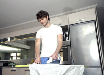 Junger Mann bügelt Hemd in der Küche zu Hause - AJOF01549