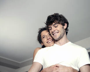 Happy woman embracing man from behind at home - AJOF01551