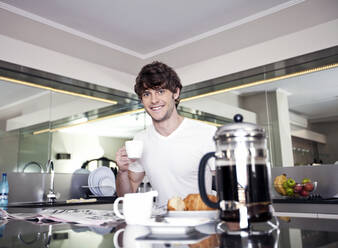 Lächelnder junger Mann beim Kaffee in der Küche - AJOF01553