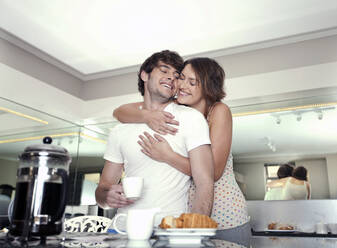 Happy woman embracing boyfriend having coffee at home - AJOF01554