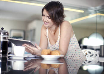 Smiling young woman using digital tablet at kitchen - AJOF01556