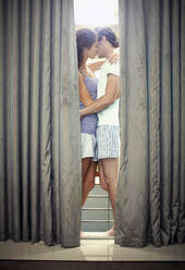 Junges Paar küsst sich hinter einem Vorhang zu Hause - AJOF01569