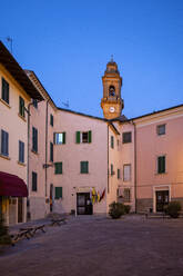 Italien, Provinz Pisa, Pomarance, Piazza de Larderel in der Abenddämmerung mit dem Glockenturm der Kirche von San Giovanni Battista im Hintergrund - MAMF01954