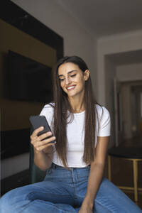 Lächelnde junge schöne Frau Text-Messaging durch Smartphone zu Hause - MTBF01075