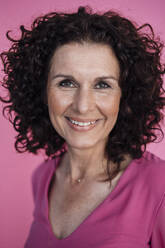Lockig behaarte Geschäftsfrau lächelnd über rosa Hintergrund - MOEF03857