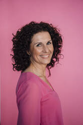 Lächelnde Geschäftsfrau stehend vor rosa Hintergrund - MOEF03858