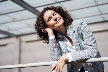 Businesswoman with eyes closed leaning on railing while day dreaming during sunny day - MOEF03865