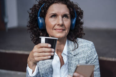 Mature businesswoman listening music while holding coffee cup - MOEF03866
