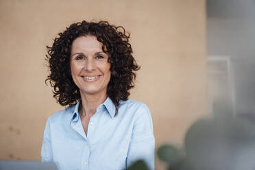 Smiling female professional with curly brown hair at office - MOEF03875