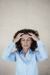 Mature female professional with hands in hair suffering from headache - MOEF03884