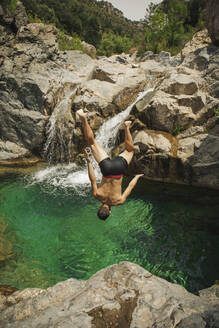 Mann ohne Hemd springt an einem sonnigen Tag in einen Wasserfall - ACPF01268