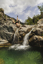 Carefree shirtless man doing somersault by waterfall - ACPF01269