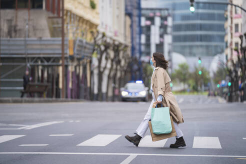 Frau überquert Straße mit Einkaufstüten während der Pandemie - SNF01508