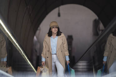 Junge Frau mit Einkaufstaschen, die auf einer Rolltreppe nach oben fährt - SNF01511