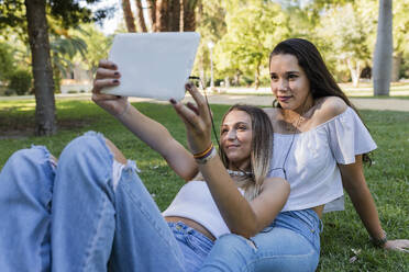 Junge Frau mit Freundin, die ein Selfie durch ein digitales Tablet im Park macht - JRVF01444