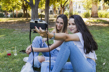 Women taking selfie through camera while sitting at public park - JRVF01445