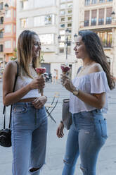 Young female friends looking at each other holding ice cream cones in city - JRVF01454