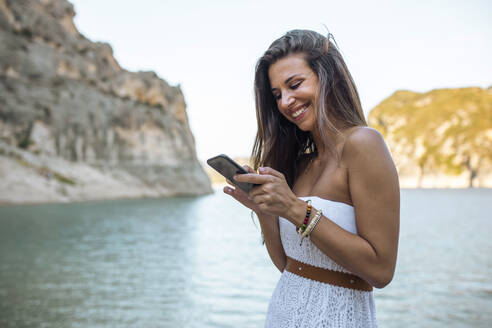 Lächelnde Frau mit Smartphone in Pantano de Santa Ana, Castillonroy, Spanien - ACPF01270