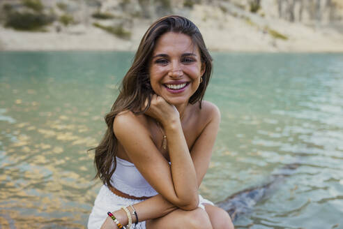 Schöne junge Frau mit Hand am Kinn, sitzend im Pantano de Santa Ana, Castillonroy, Spanien - ACPF01272