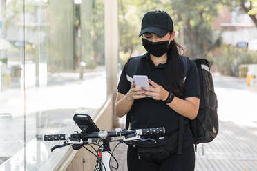 Female delivery person wearing protective face mask using smart phone - JRVF01459