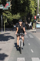 Junge weibliche Mitarbeiterin eines wichtigen Dienstes fährt mit dem Fahrrad auf der Straße an einem sonnigen Tag - JRVF01461