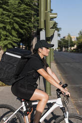 Weiblicher Zusteller auf dem Fahrrad an einem sonnigen Tag - JRVF01462