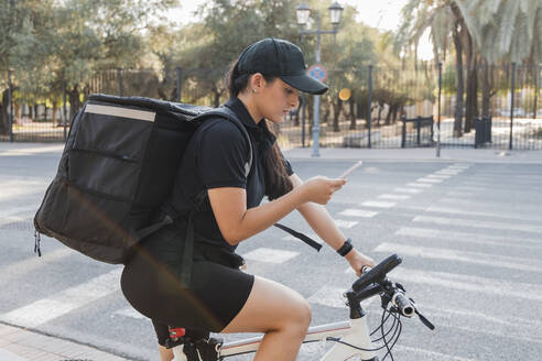 Weibliche Entbindungspflegerin benutzt ihr Smartphone, während sie auf dem Fahrrad sitzt - JRVF01467