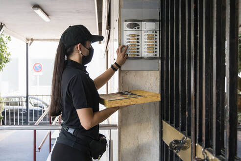 Junge Pizzalieferantin hält Schachtel, während sie während der Pandemie an der Tür klingelt - JRVF01471