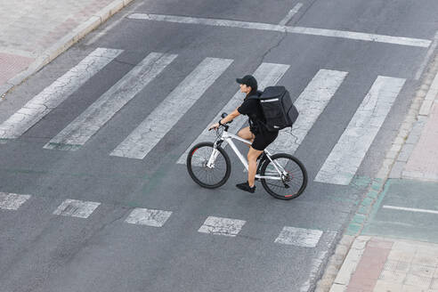 Weiblicher Zusteller mit Rucksack auf dem Fahrrad an einer Kreuzung - JRVF01483