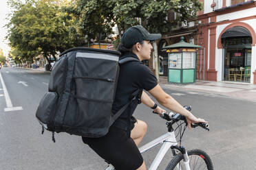 Weibliche Lieferperson mit Rucksack auf dem Fahrrad auf der Straße - JRVF01494