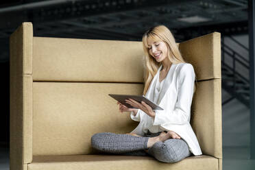 Junge Frau, die im Schneidersitz ein digitales Tablet benutzt - PESF03092