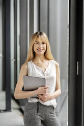 Businesswoman holding laptop at workplace - PESF03101