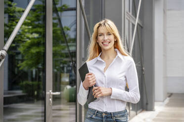 Smiling businesswoman holding digital tablet while standing in front of building - PESF03119