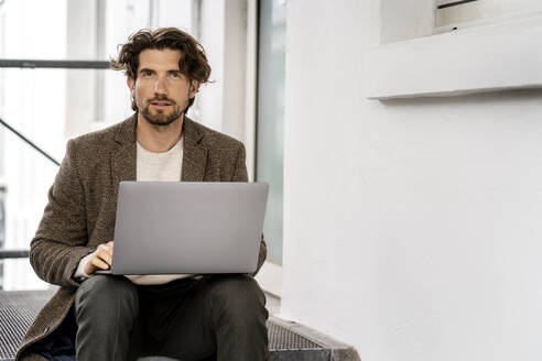 Männlicher Berufstätiger mit Laptop auf Stufen sitzend - PESF03125