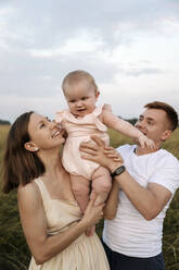 Happy mother and father carrying toddler girl at sunset - EYAF01712