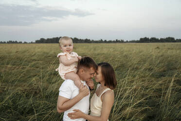 Affectionate parents embracing while carrying daughter on shoulders - EYAF01714