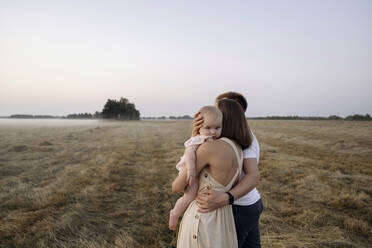 Mother carrying cute girl while standing by man in field - EYAF01719